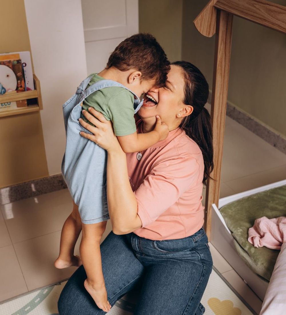 Mãe abraçando o filho sorrindo num quarto infantil colorido